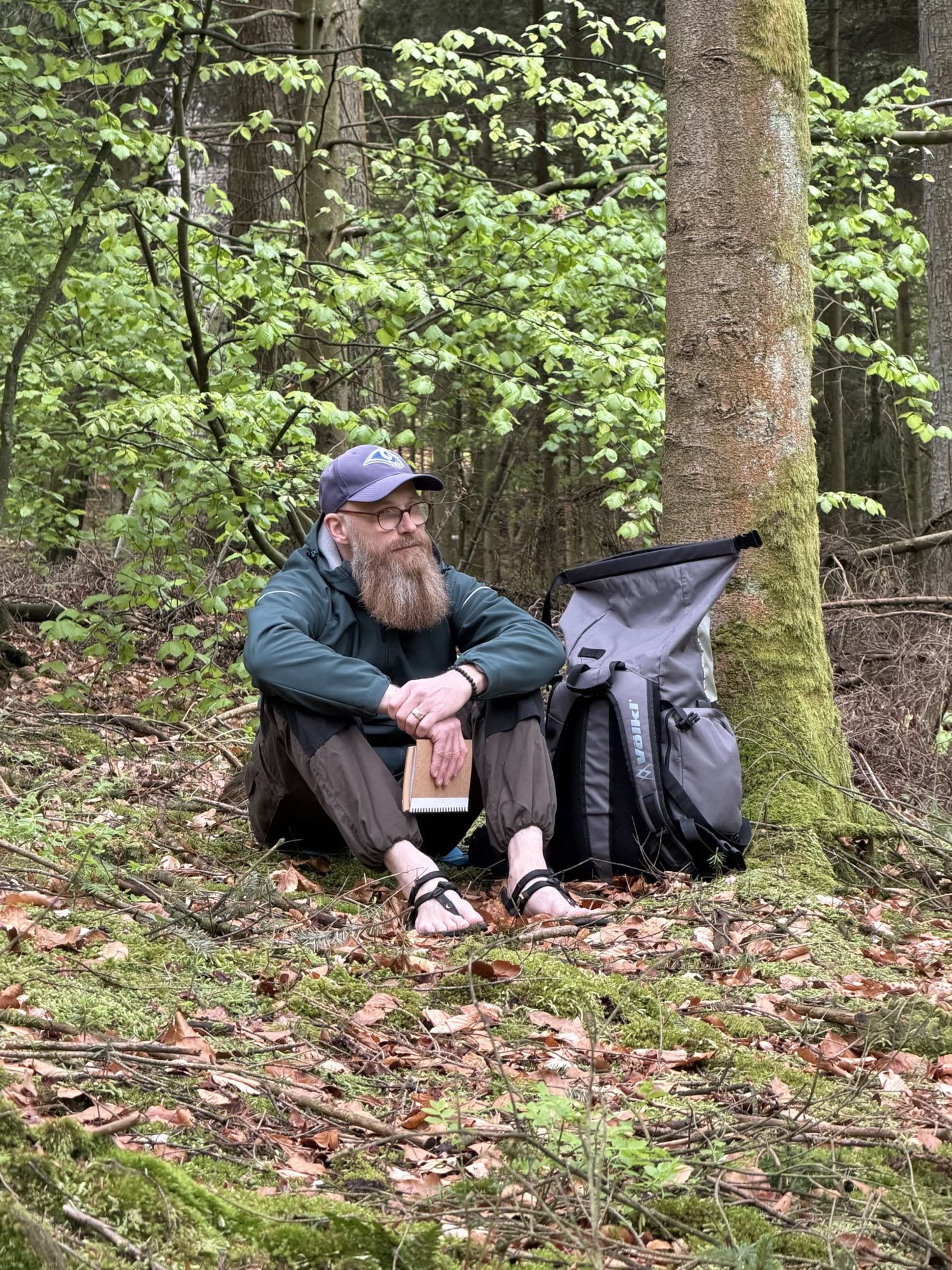 Thorsten Weber sitzt auf dem Waldboden an einen Baum gelehnt.